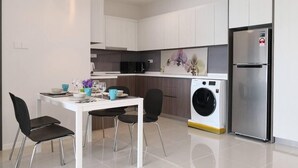 Una cocina moderna con armarios blancos, un refrigerador de acero inoxidable, una lavadora y un comedor con mesa y sillas.