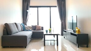 Una sala de estar moderna con un sofá seccional gris, una mesa de centro, un televisor sobre un soporte negro y un pequeño objeto decorativo sobre el soporte.