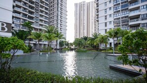 Un immeuble résidentiel moderne à plusieurs étages, entouré d’un espace paysager avec des éléments d’eau et de la verdure.