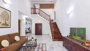 A spacious living room with a wooden staircase, a sofa, a coffee table, and a TV on a stand. - A Spacious 4BR Home Nearby Kiara Hill, Mont Kiara, Pavilion Damansara Heights (Kuala Lumpur)