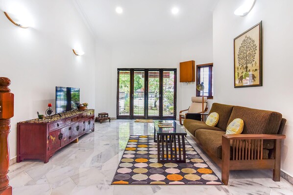 A spacious living room with a sofa, a coffee table, and a cabinet. There is a large window with a view of greenery outside.