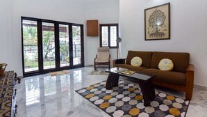 A living room with a sofa, coffee table, and a patterned rug. There is a chair and a television on the wall. - A Spacious 4BR Home Nearby Kiara Hill, Mont Kiara, Pavilion Damansara Heights (Kuala Lumpur)