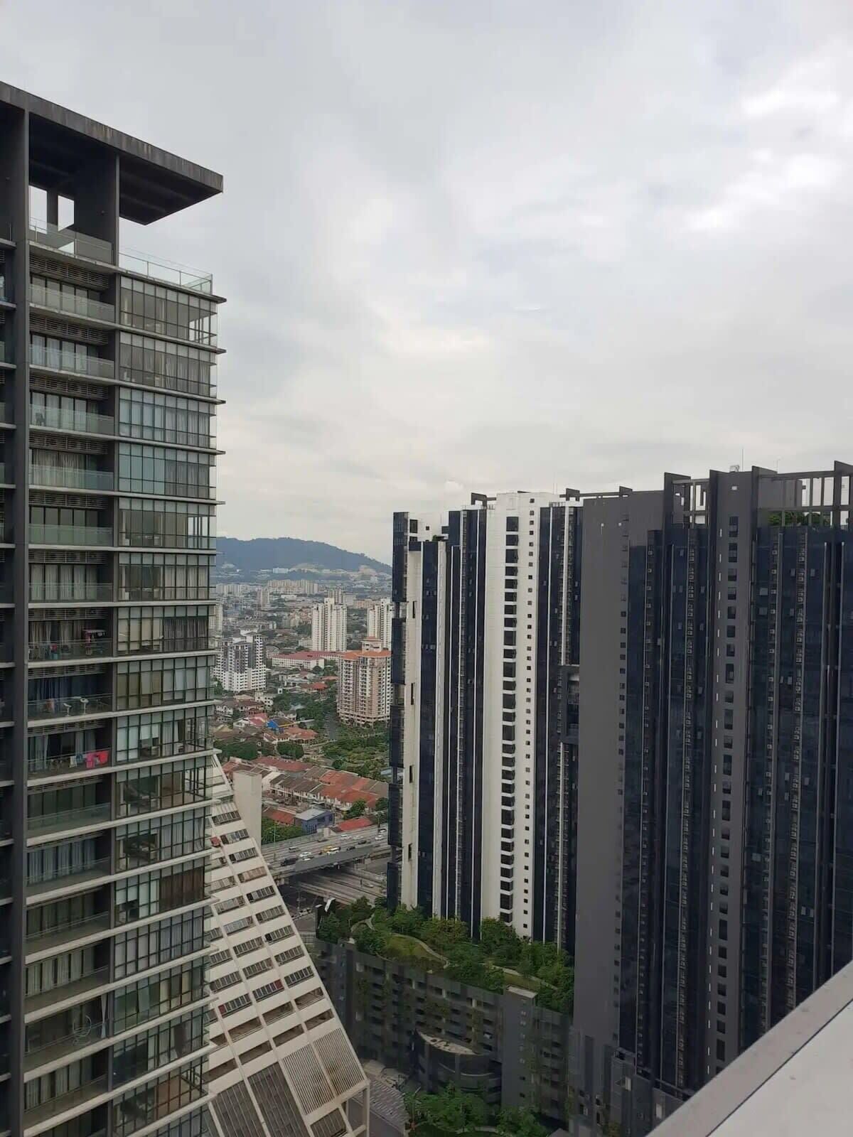 Un edificio de gran altura con varios pisos y ventanas amplias, rodeado de otros edificios altos y una vista distante de un paisaje urbano.
