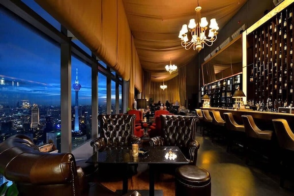 A high-rise bar with leather seating, a city view, and a bar area with shelves of bottles.