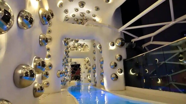 Un espace piscine intérieur moderne, doté d’un design géométrique, avec un chemin central menant à une porte.