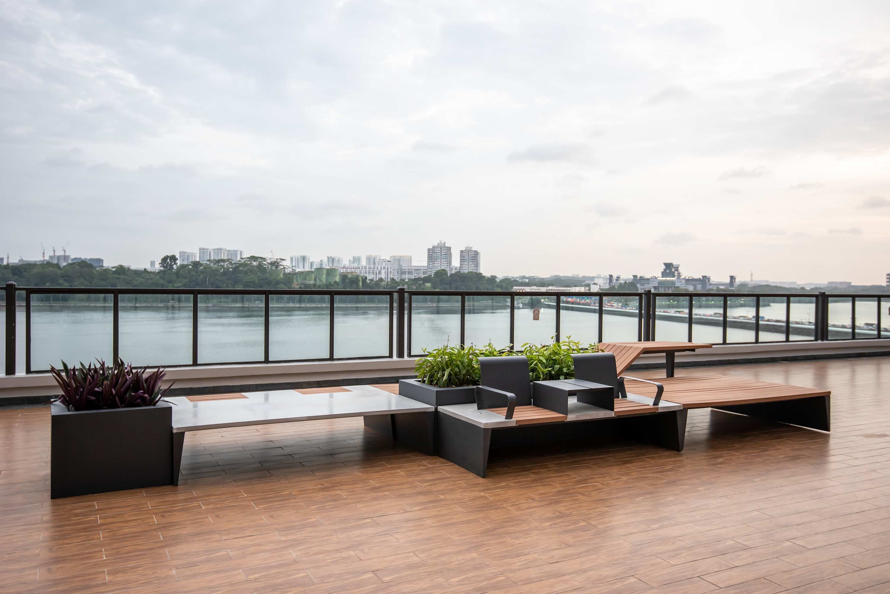 Un espace extérieur moderne, aménagé pour se détendre, avec vue sur les gratte-ciel d’une ville et sur une étendue d’eau.