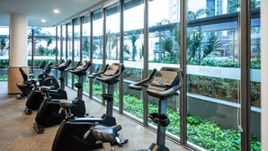 A gym with multiple stationary bikes and a large window with a view of greenery and buildings. - 2BR R&F Phase2, CIQ R&F Mall, Free Parking (Johor Bahru)