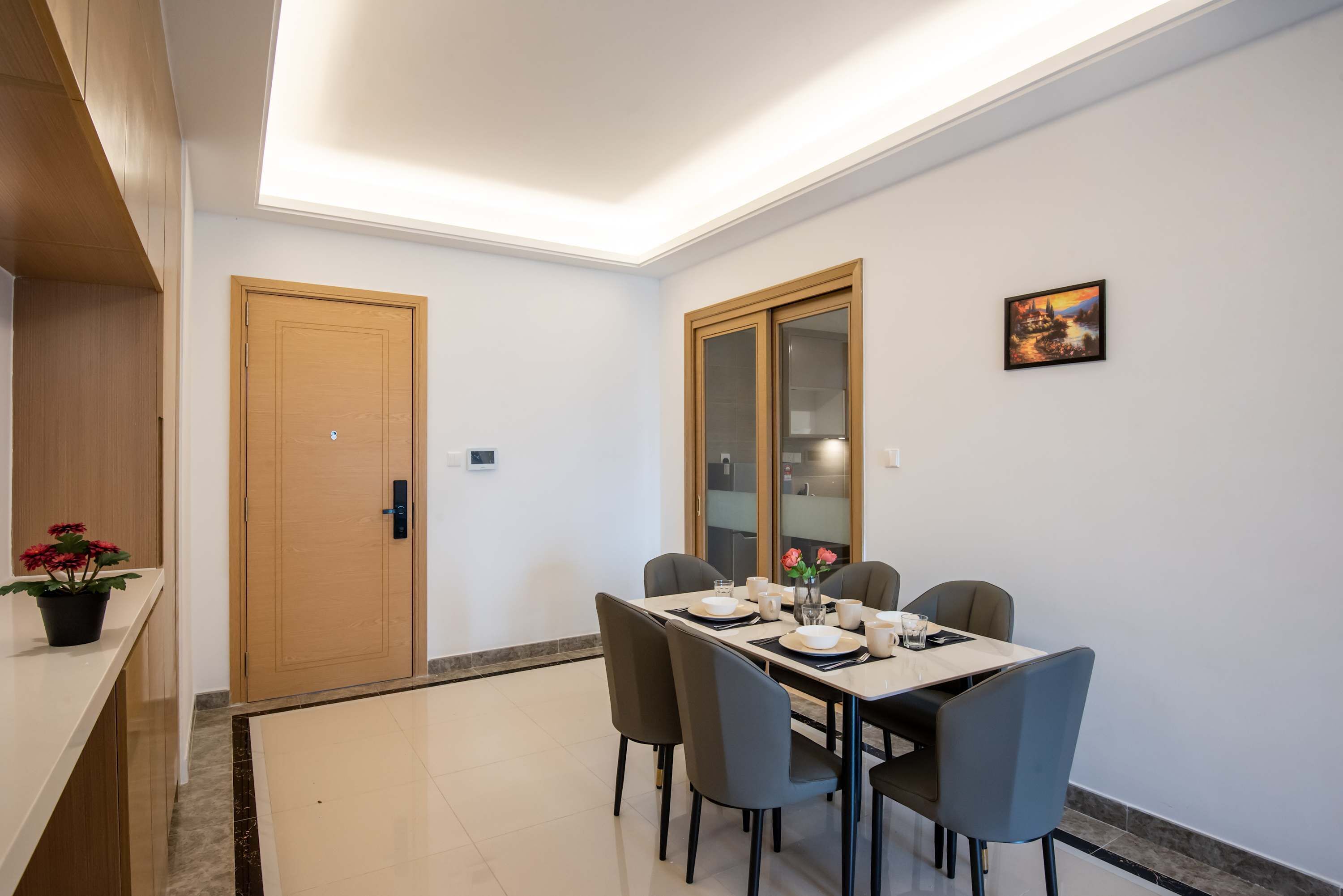 A dining area with a table set for four, a wooden door, and a framed picture on the wall.
