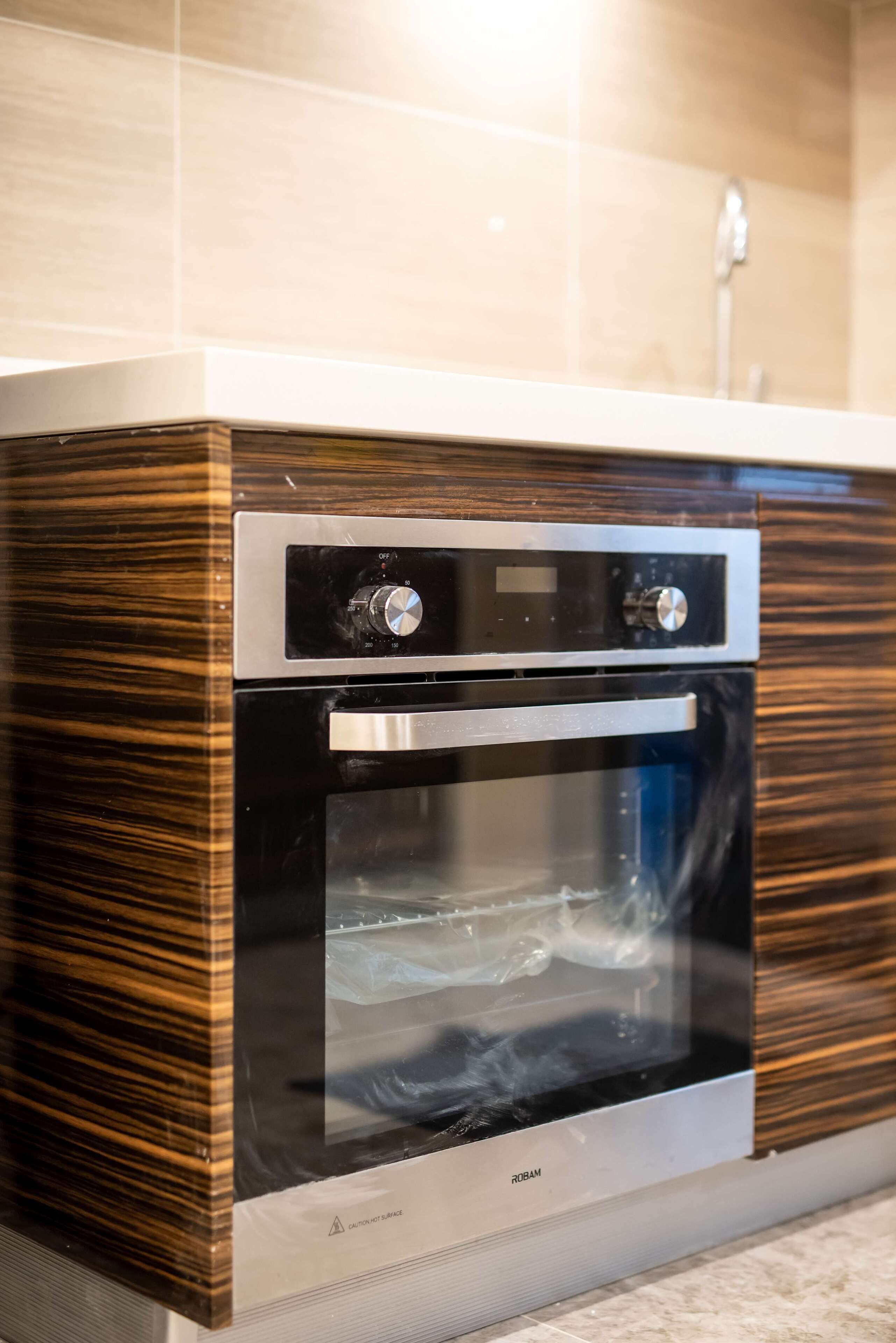 A modern kitchen with a built-in oven and microwave, featuring a sleek design and a wooden finish.