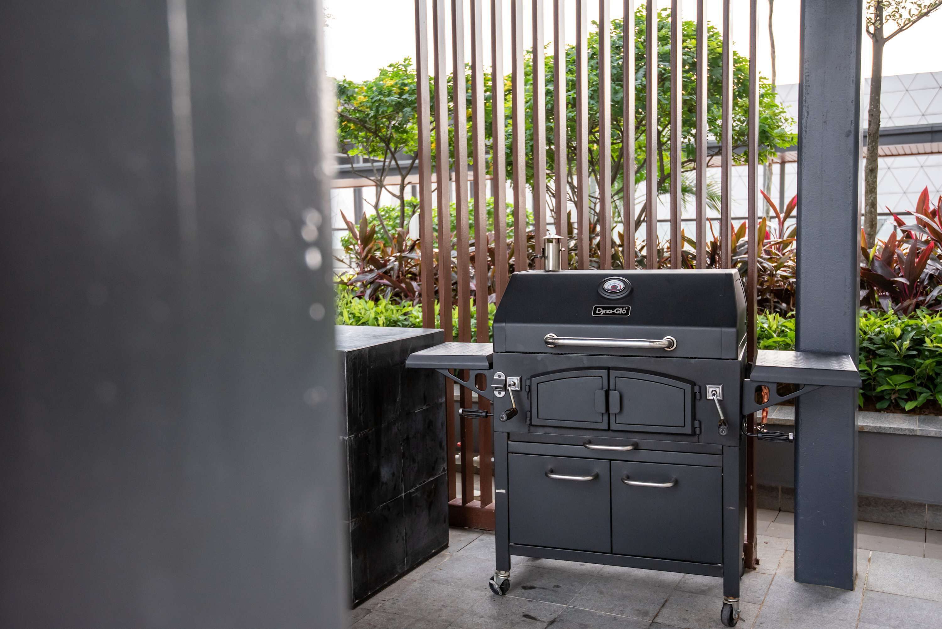 A portable grill with a digital display, positioned in an outdoor patio area with a view of greenery and a metal fence.