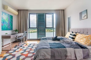 A bedroom with a bed, a desk, a chair, a large window, and a view of the outdoors.