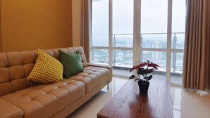 A modern living room with a leather sofa, a wooden coffee table, and a large window offering a city view.