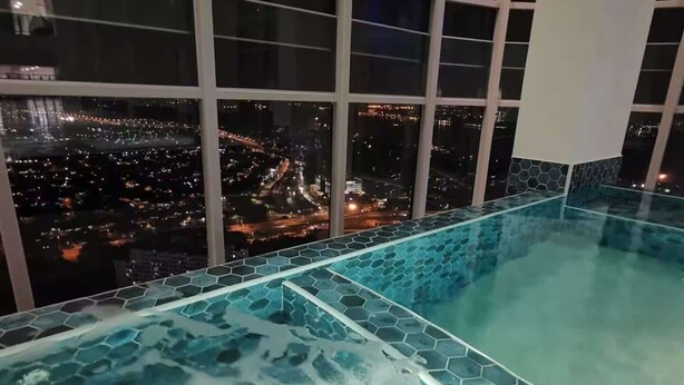 A rooftop infinity pool with a hexagonal tile design, overlooking a cityscape at night.