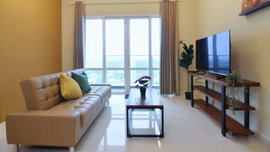 A modern living room with a sofa, a coffee table, a TV on a wooden stand, and a large window with curtains.