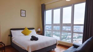A hotel room with a large window offering a city view, a bed with white bedding and a yellow pillow, and a black leather sofa.
