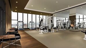 A modern gym with exercise equipment, large windows, and a view of the city.