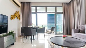 Una sala de estar moderna con un televisor de pantalla plana, un comedor con mesa y sillas, un sofá y un balcón con cortinas.