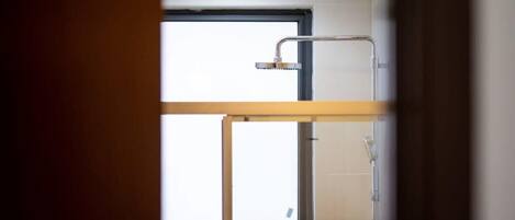 Une salle de bain moderne avec une douche à l’italienne en verre, une fenêtre et des toilettes apparentes.