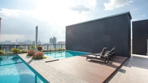 Un espace piscine sur le toit, doté de chaises longues, offrant une vue dégagée sur les gratte-ciel de la ville et présentant une architecture moderne.