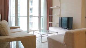 A modern living room with a sofa, a glass coffee table, and a flat-screen TV on a white cabinet. - Central 2BR Apt 5 Mins Klcc Twin Towers, Bathtub (Kuala Lumpur)