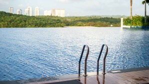 Una piscina con barandillas metálicas, rodeada de vegetación y edificios al fondo.
