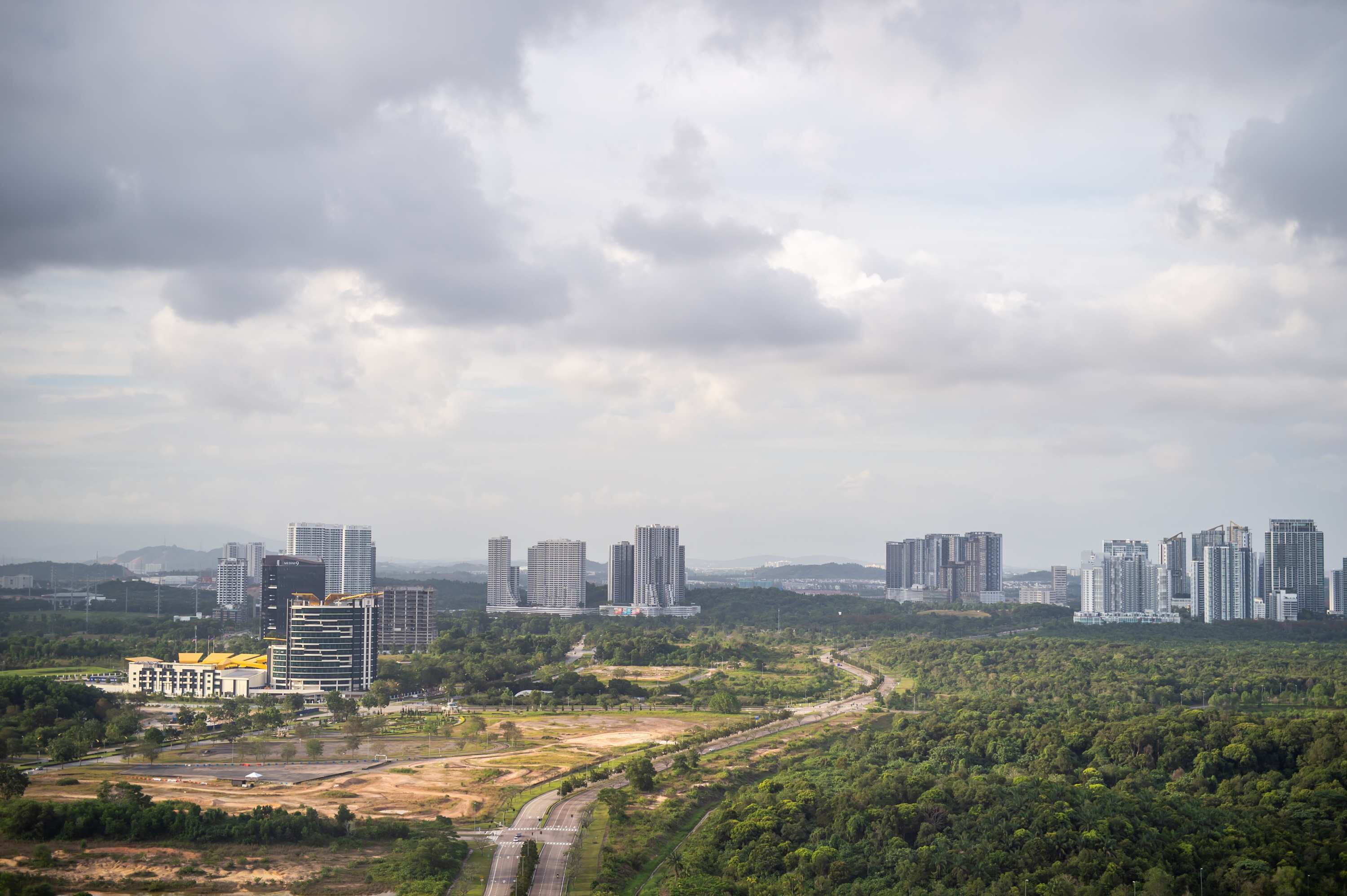 A cityscape with modern high-rise buildings and a dense green forest area.