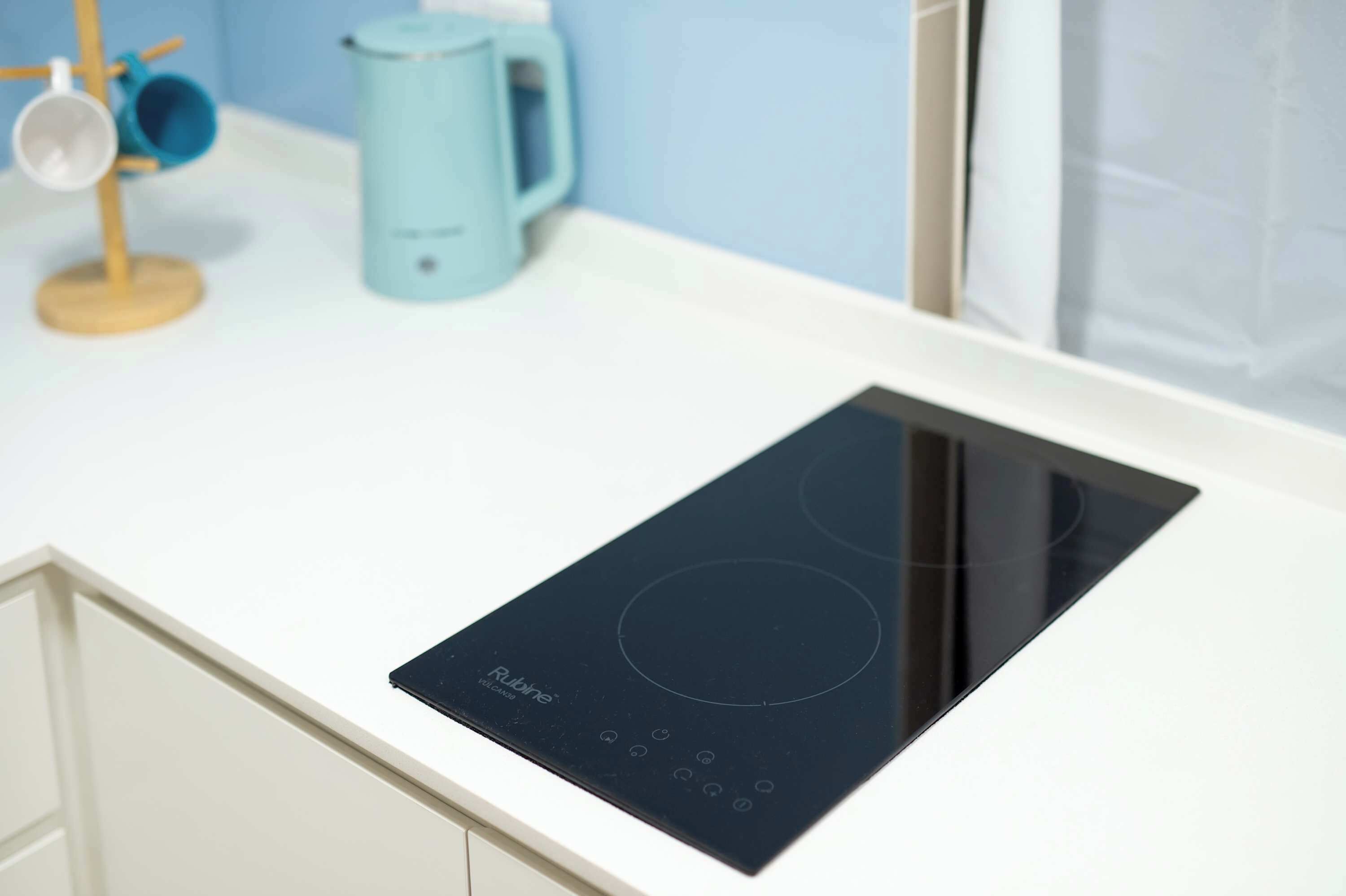 A modern kitchen with a black induction cooktop, a light blue kettle, and a wooden spoon holder.