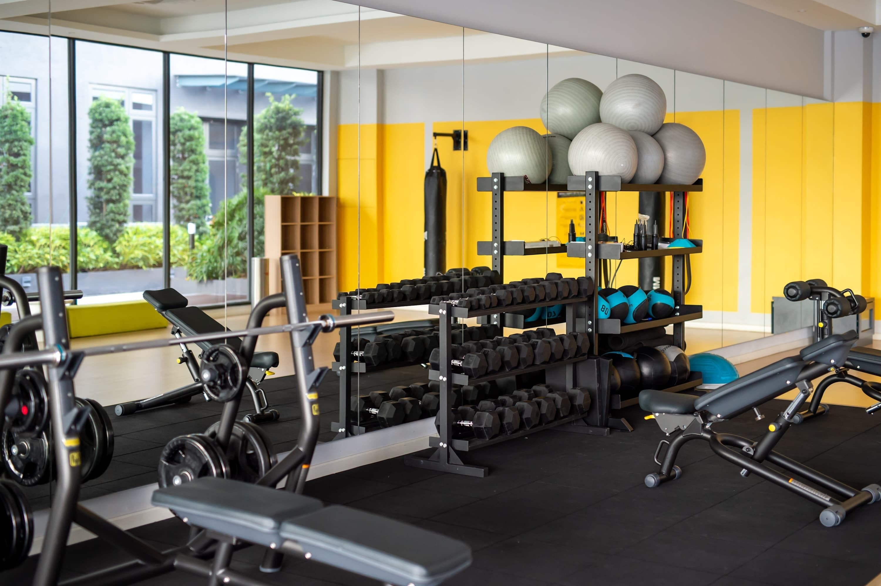 Un gimnasio con equipamiento para levantamiento de pesas, pelotas de ejercicio y mancuernas.