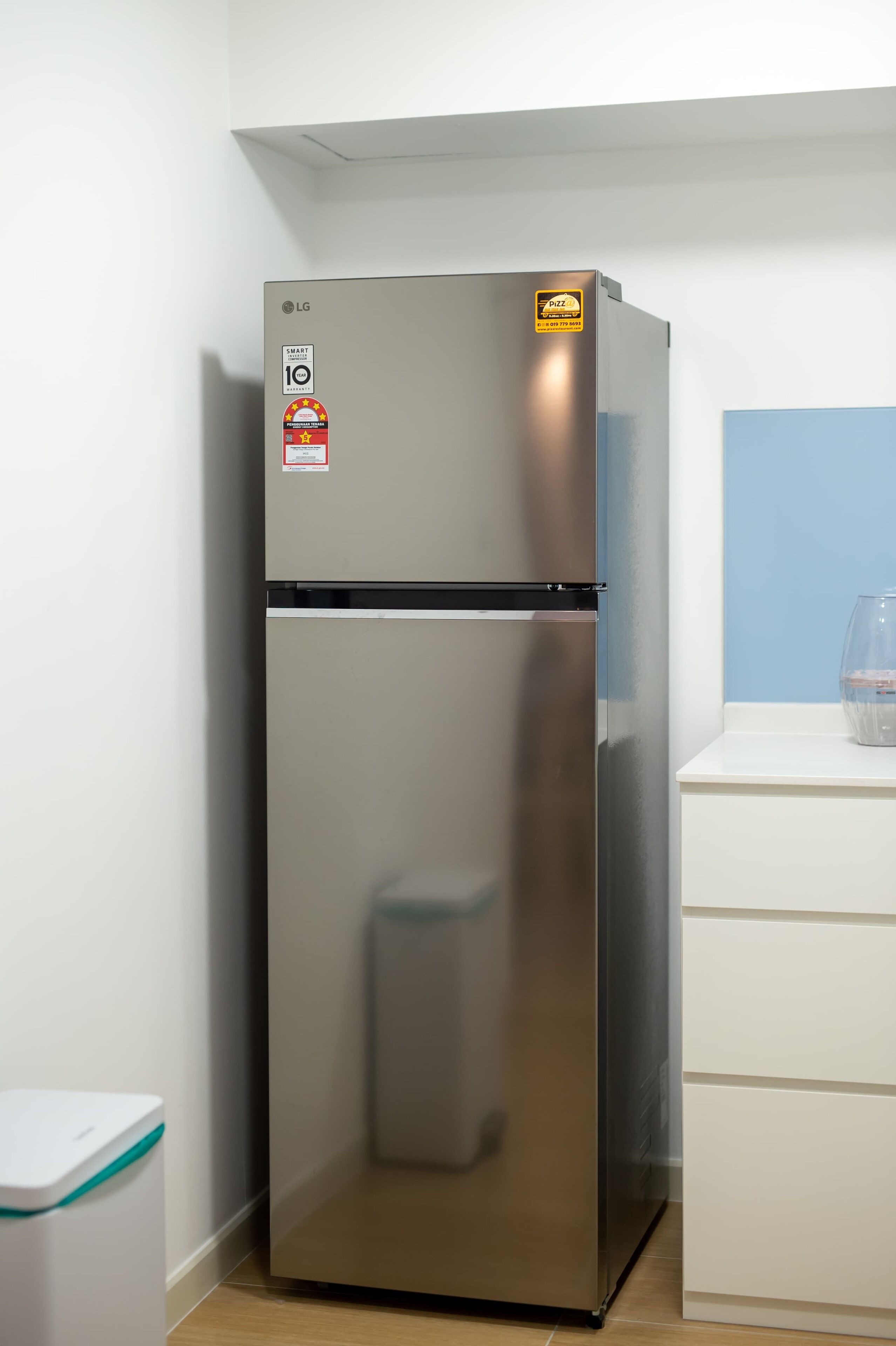 A stainless steel refrigerator with a pizza logo sticker, a smart home certification, and a black control panel.