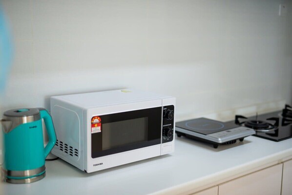 Un four à micro-ondes blanc est posé sur un plan de travail de cuisine, avec une bouilloire turquoise à côté.