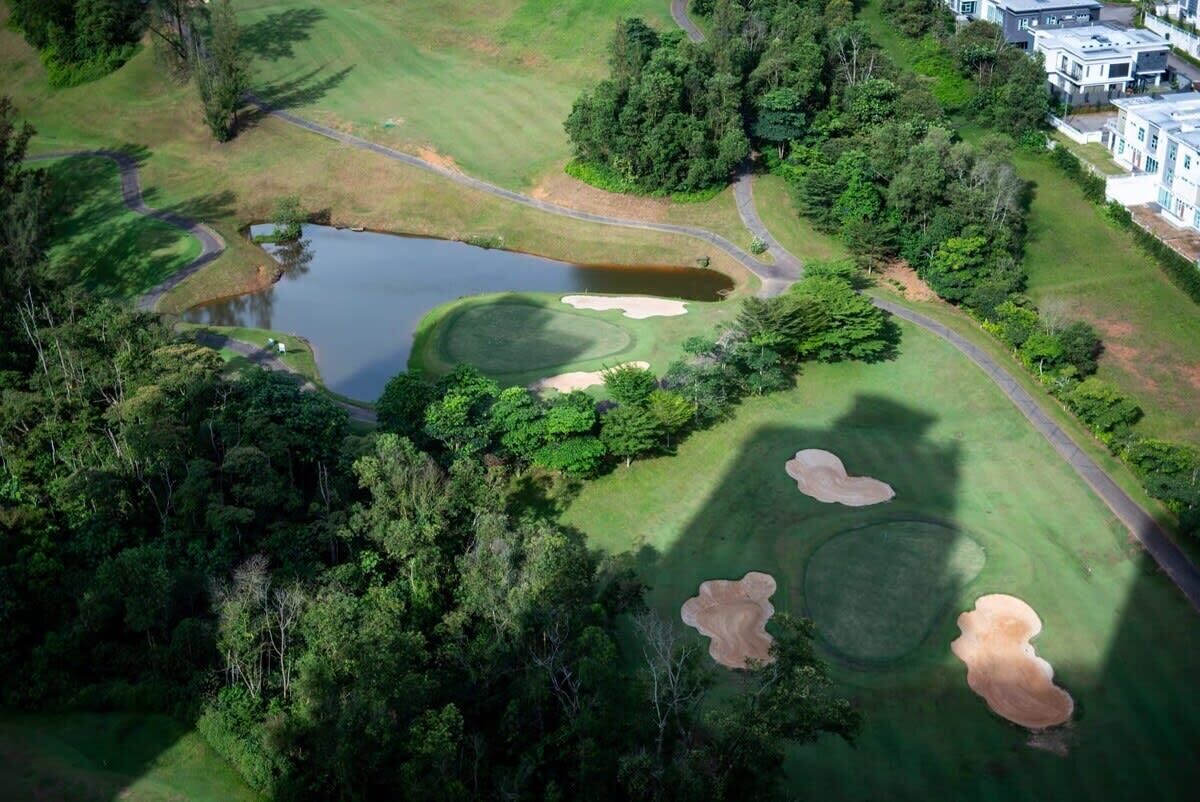 An aerial view of a golf course with sand bunkers, a pond, and surrounding greenery.