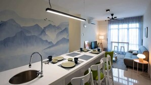 Een moderne keuken met een centraal eiland, een eethoek met stoelen, en een woonkamer met een bank en een lamp.