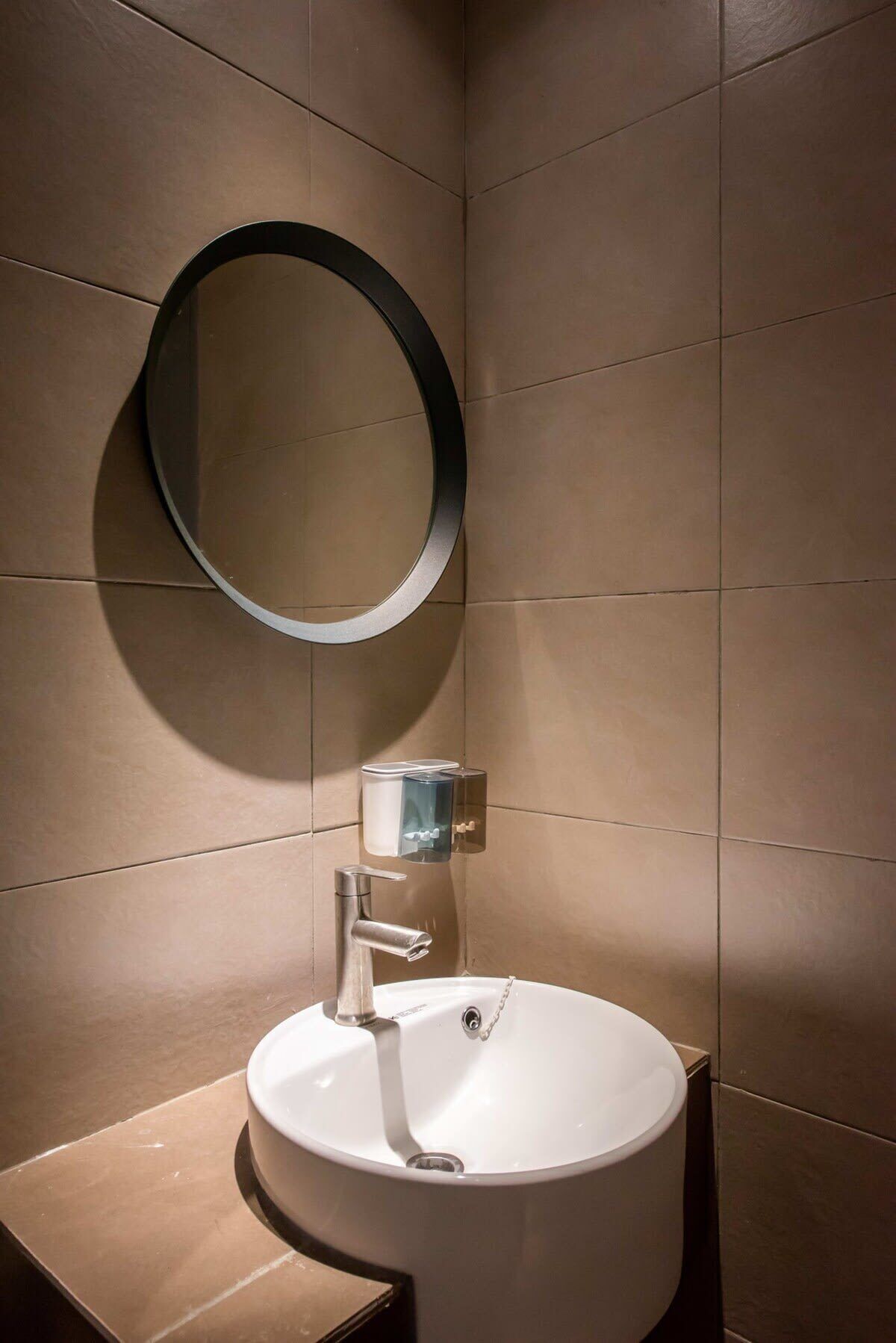 A modern bathroom with a round mirror, a white sink, and a soap dispenser.
