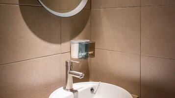 A modern bathroom with a round mirror, a white sink, and a soap dispenser.