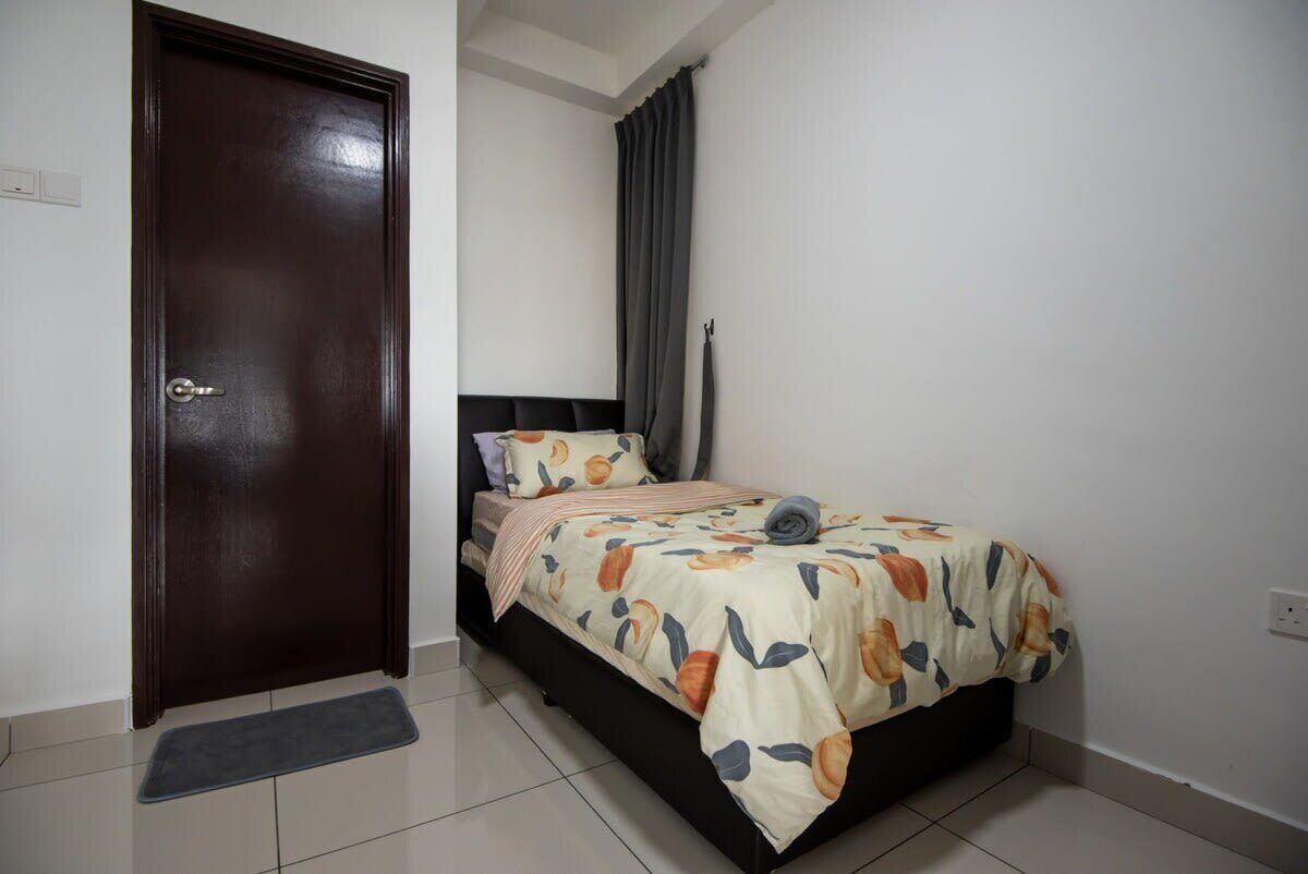 A bedroom with a dark wooden door, a bed with a floral bedspread, a bedside table, and a grey rug.