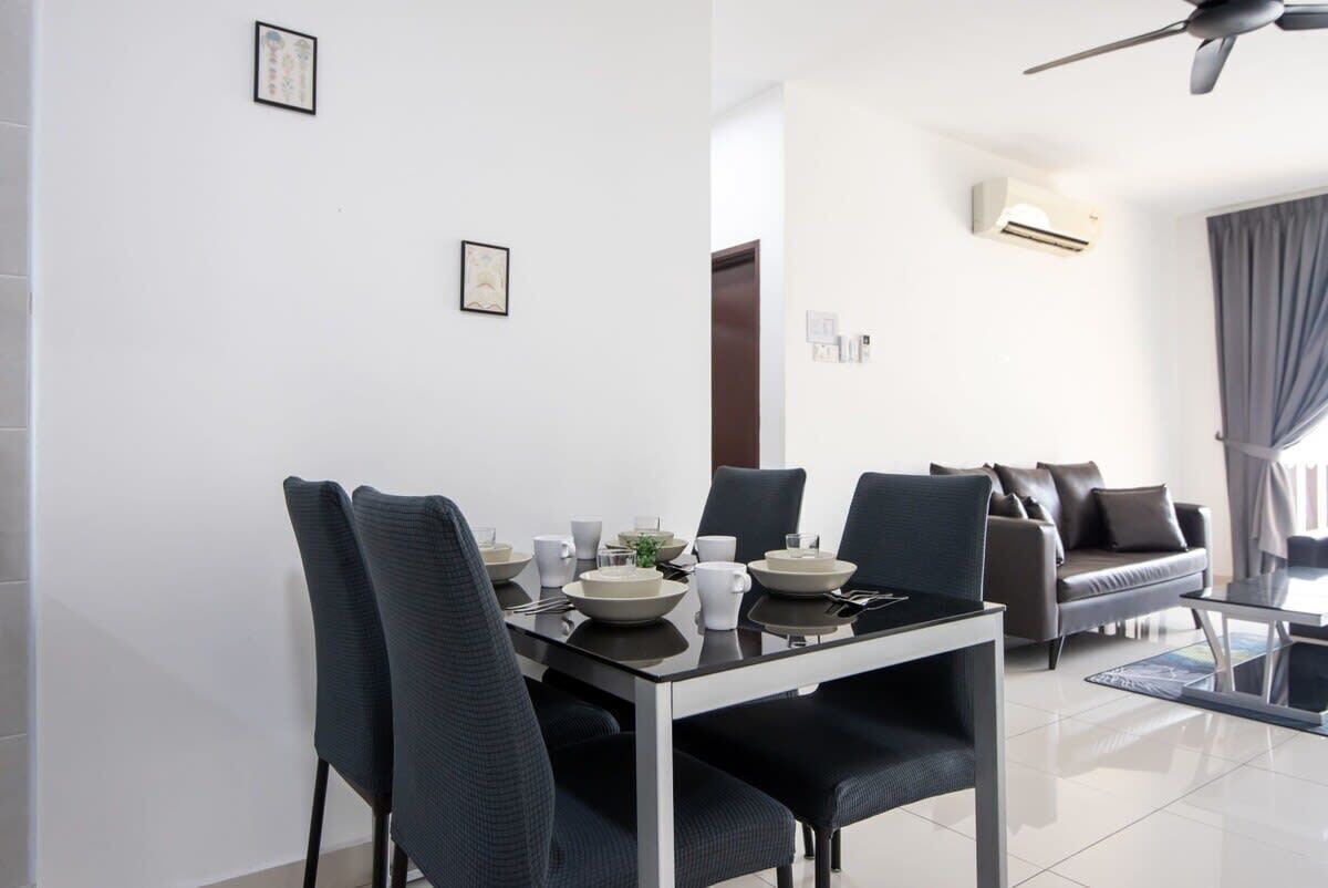 A modern dining area with a glass-top table, black chairs, and a sofa in the background.