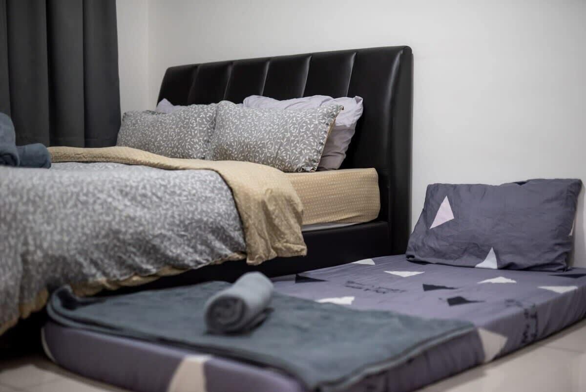 A bed with a black headboard, grey and white patterned pillows, and a rolled-up blanket on the floor.