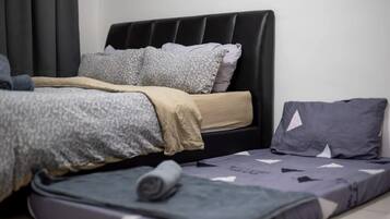 A bed with a black headboard, grey and white patterned pillows, and a rolled-up blanket on the floor.