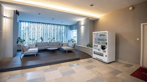 Un vestíbulo moderno con zona de estar, máquina expendedora y vista a través de una ventana con diseño.