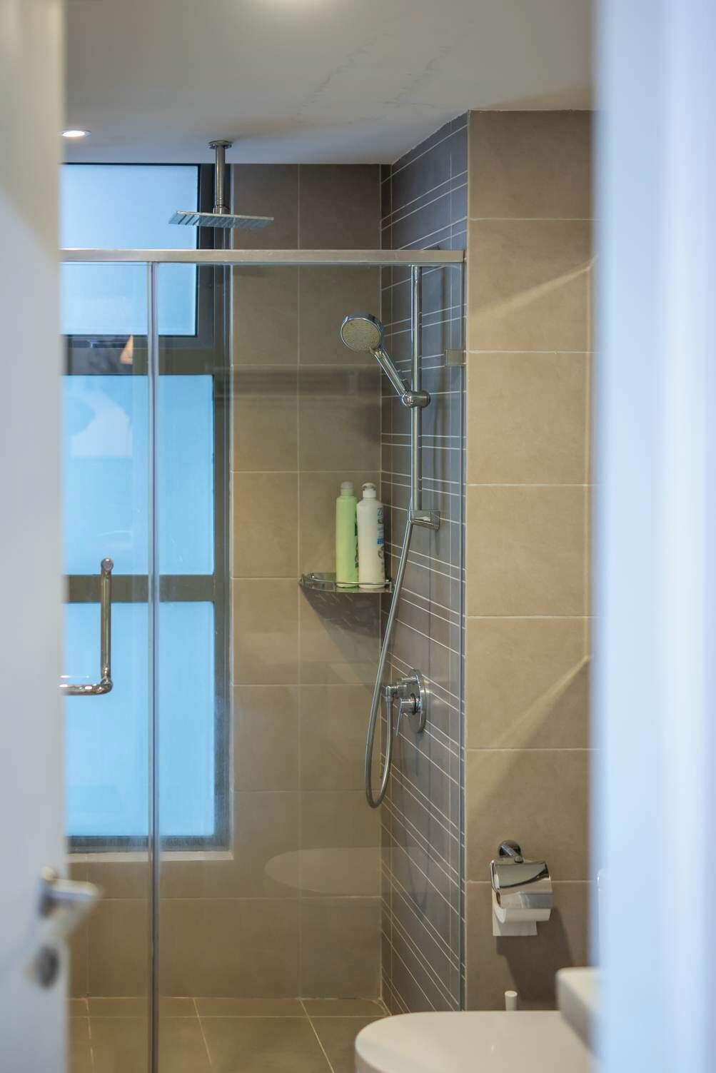 Un baño moderno con cabina de ducha de vidrio, un inodoro y un estante con artículos de aseo.