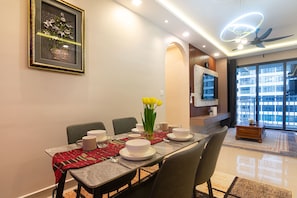 A modern dining area with a long table set for four, a vase of yellow flowers, and a television mounted on the wall. - 3BR Lsh33 KL Duke Highway Genting Free parking (Kuala Lumpur)