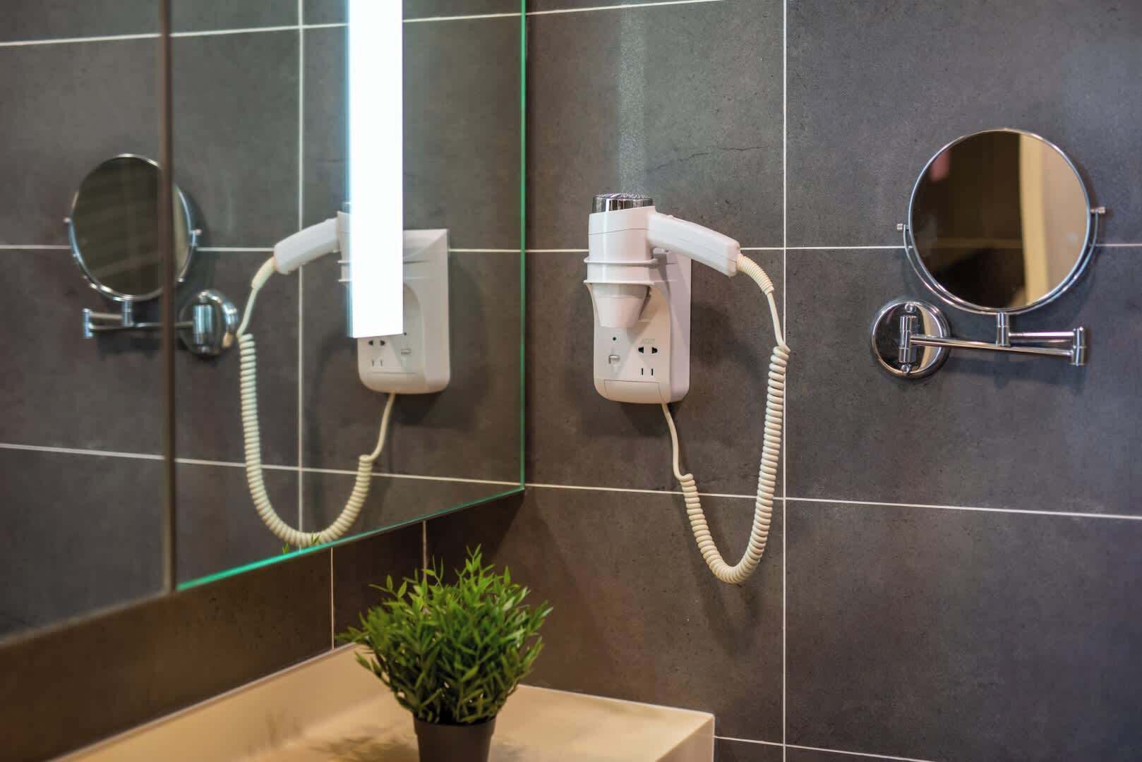 Casa de banho com secador de cabelo fixado na parede, espelho e uma pequena planta num vaso.