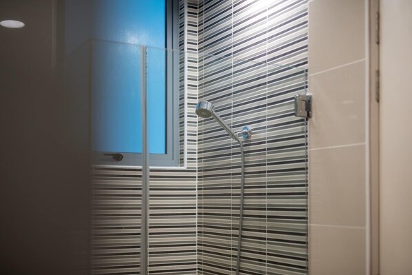 Una ducha con ventanal vertical y azulejos de pared a rayas.