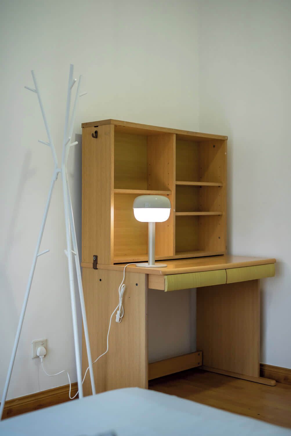 Un escritorio de madera con una lámpara de escritorio blanca, un enchufe y una silla blanca.