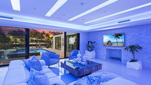 Un salon moderne avec un grand canapé, des fauteuils bleus, une table basse et un téléviseur fixé à un mur en briques.