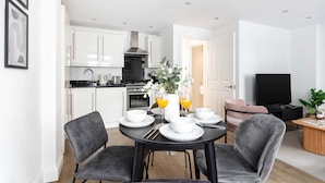 A modern kitchen with white cabinets, a black stove, and a stainless steel range hood. - Lovely 1BR near Big Ben & Buckingham Palace (London)