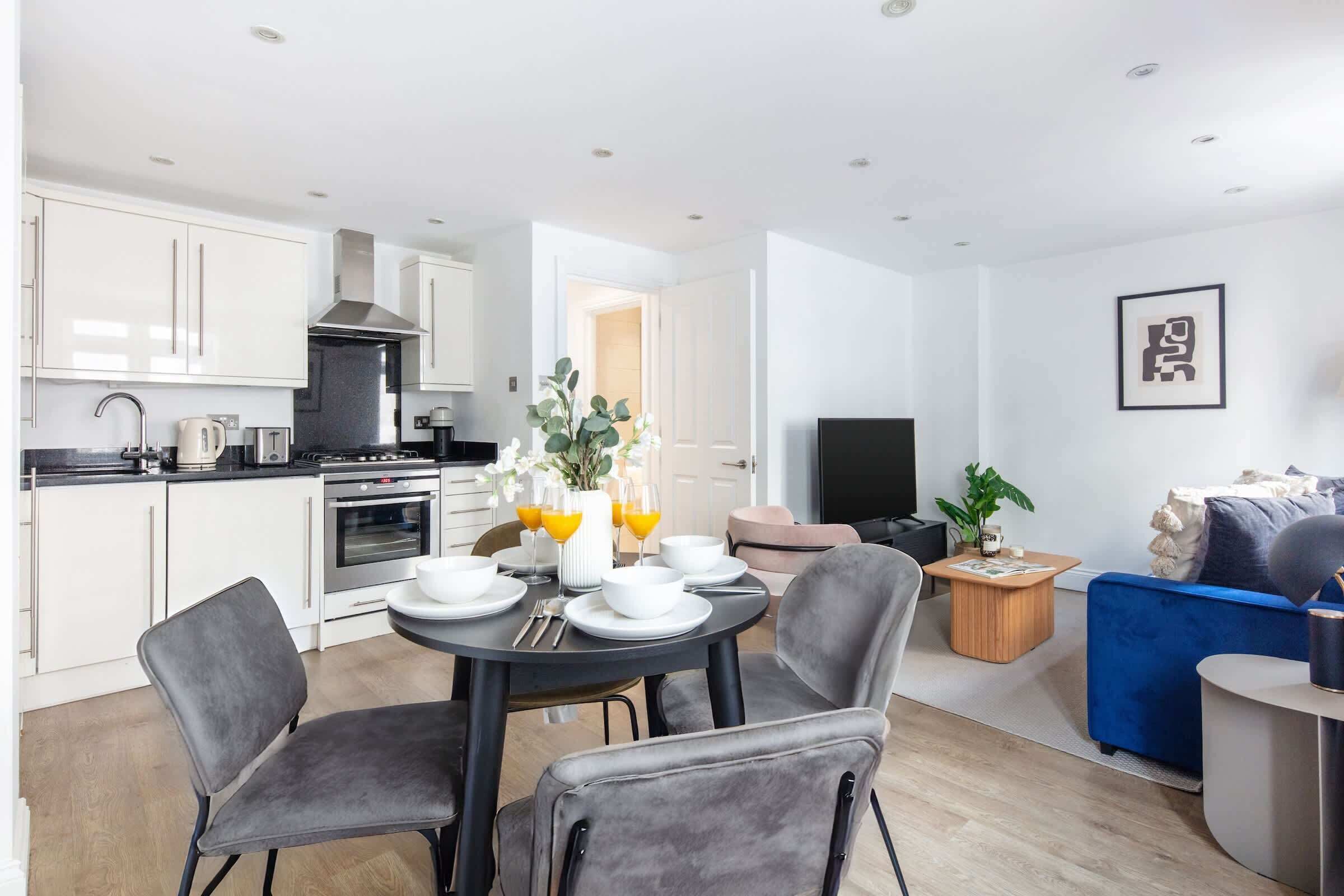 A modern kitchen with white cabinets, a black stove, and a dining area with a round table and four chairs.
