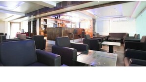 A modern lounge area with sofas and tables, a reception desk, and a bar area with shelves. - Hotel Sunland (Baramati)