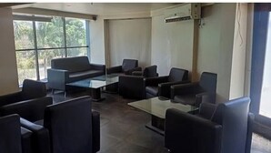 A conference room with a glass table, black chairs, and a large window with a view of trees. - Hotel Sunland (Baramati)