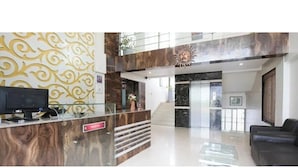 A reception area with a marble reception desk, a black leather sofa, and a staircase leading to an upper level. - Hotel Sunland (Baramati)
